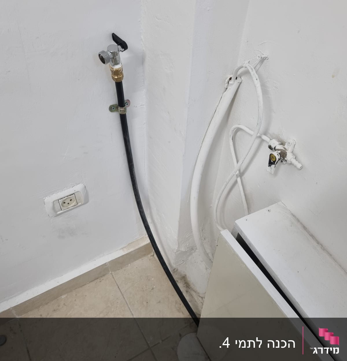 ברז מים מחובר לצינור שחור על קיר לבן